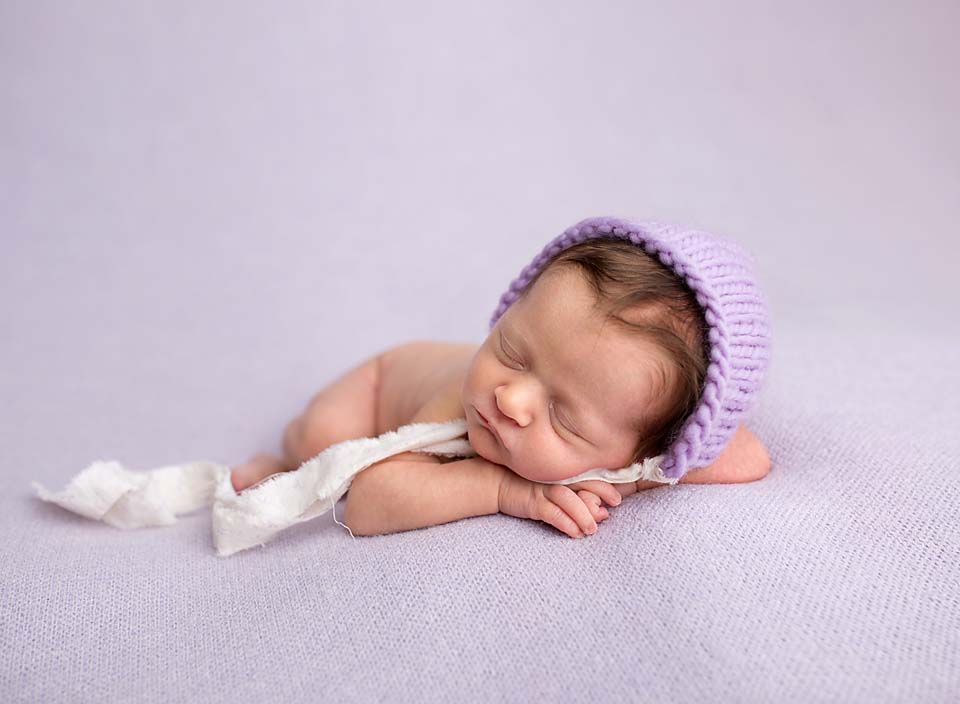 Sleeping newborn on purple blanket with bonnet, professional newborn photography serving Uxbridge