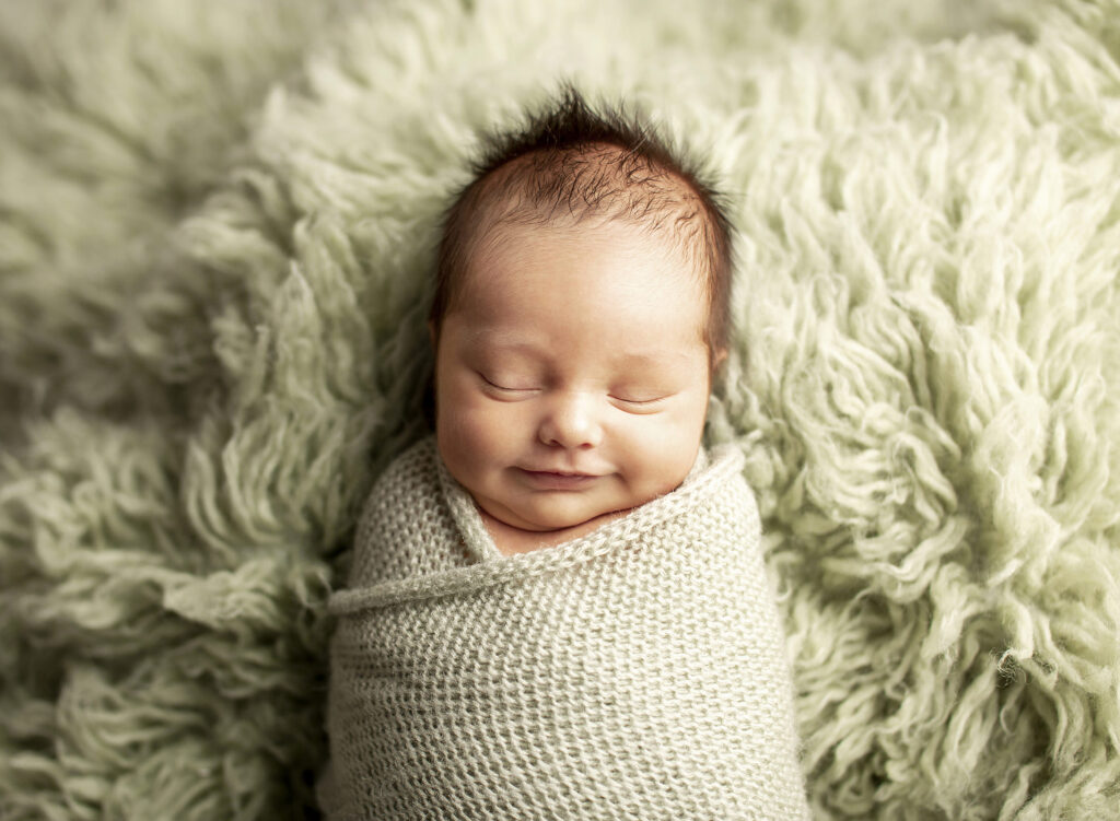Swaddled newborn smiling at newborn portrait session
